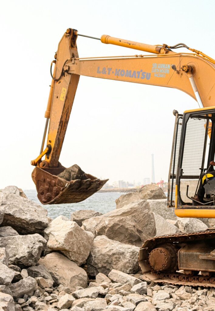 A large excavator moving rocks at an outdoor construction site near water.