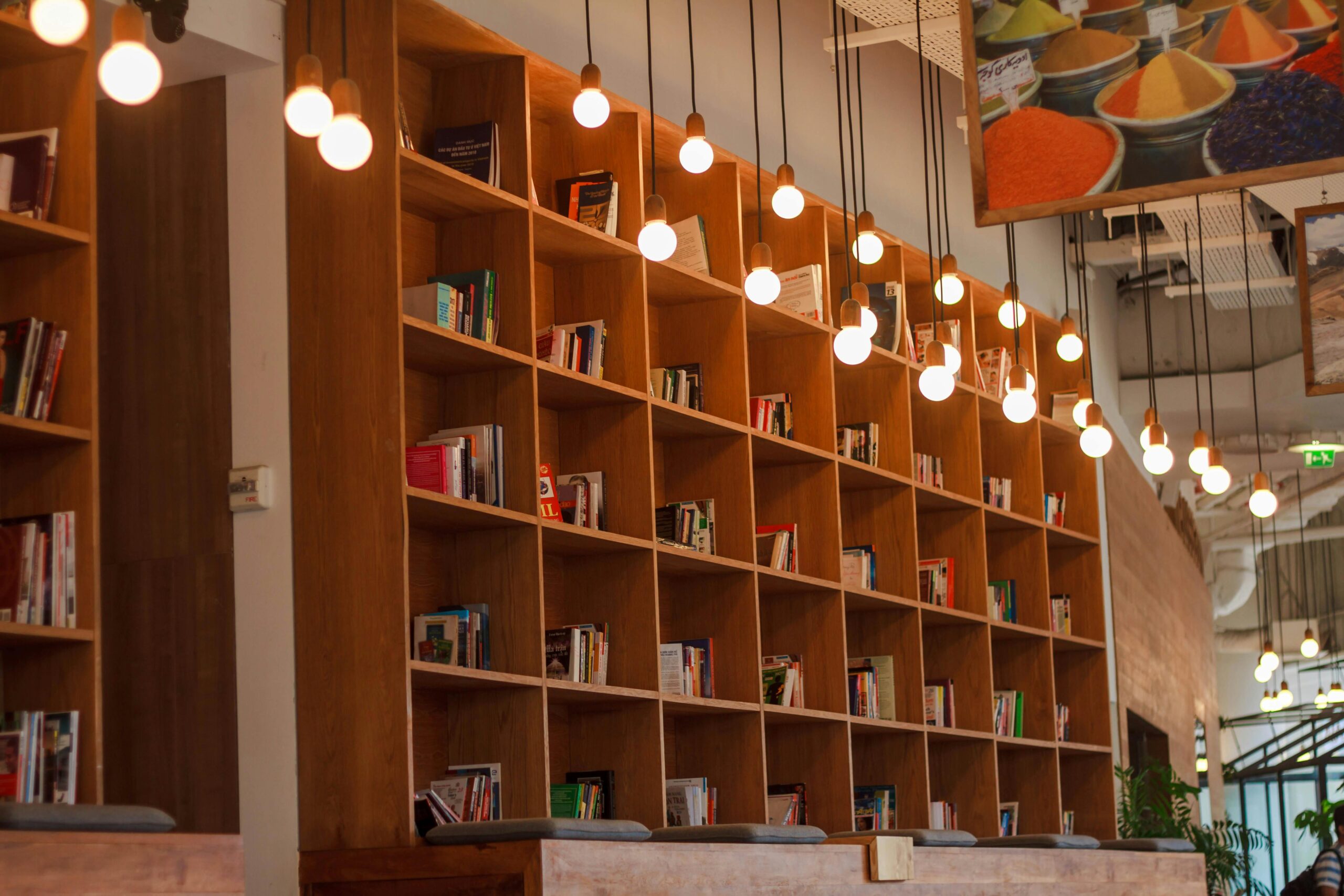 Spacious library with wooden bookshelves and hanging lights in a modern setting.